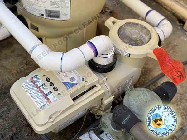 Close-up view of a new pool pump installation by Walnut Creek Pool Cleaning Service, featuring a modern pump with clear labeling and secure PVC piping connections. A tag is visible, indicating recent servicing or a safety check on the equipment.